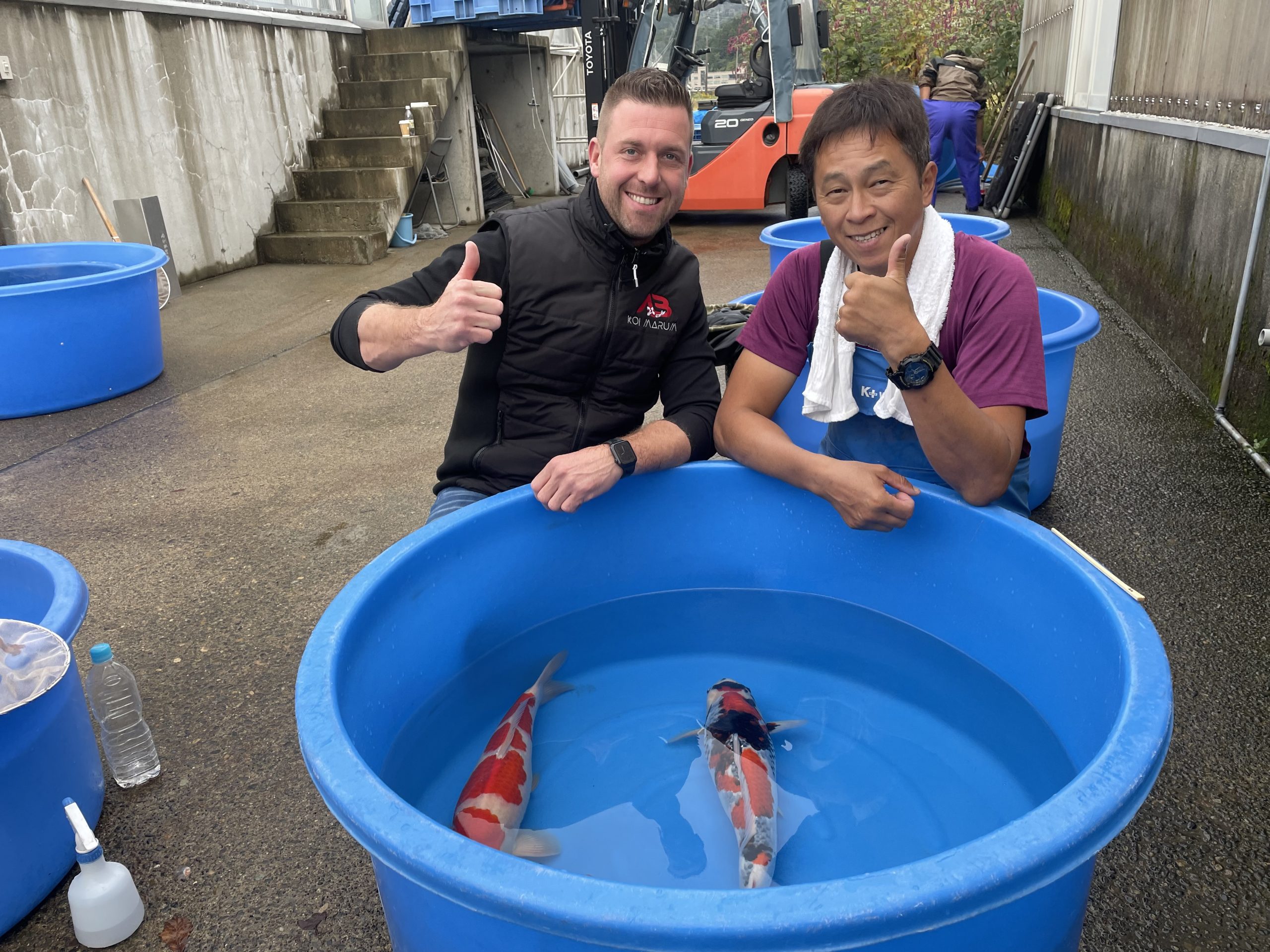 Arjan en een Japanse kweker samen bij een blauwe bak met koi